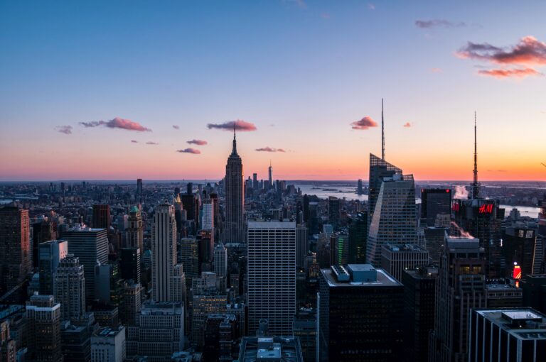 Silhouette de la ville au coucher du soleil à New York, avec des gratte-ciel illuminés et le ciel orangé en arrière-plan.